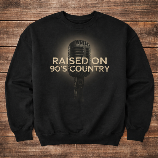 Black sweatshirt with a microphone graphic and 'Raised on 90's Country' text on a wooden surface
