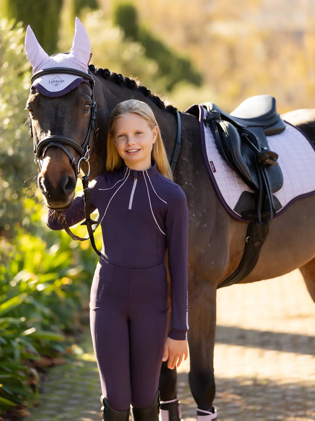 Junior rider wearing LeMieux Juniper purple pull-on breeches with a full-seat silicone grip and side phone pocket