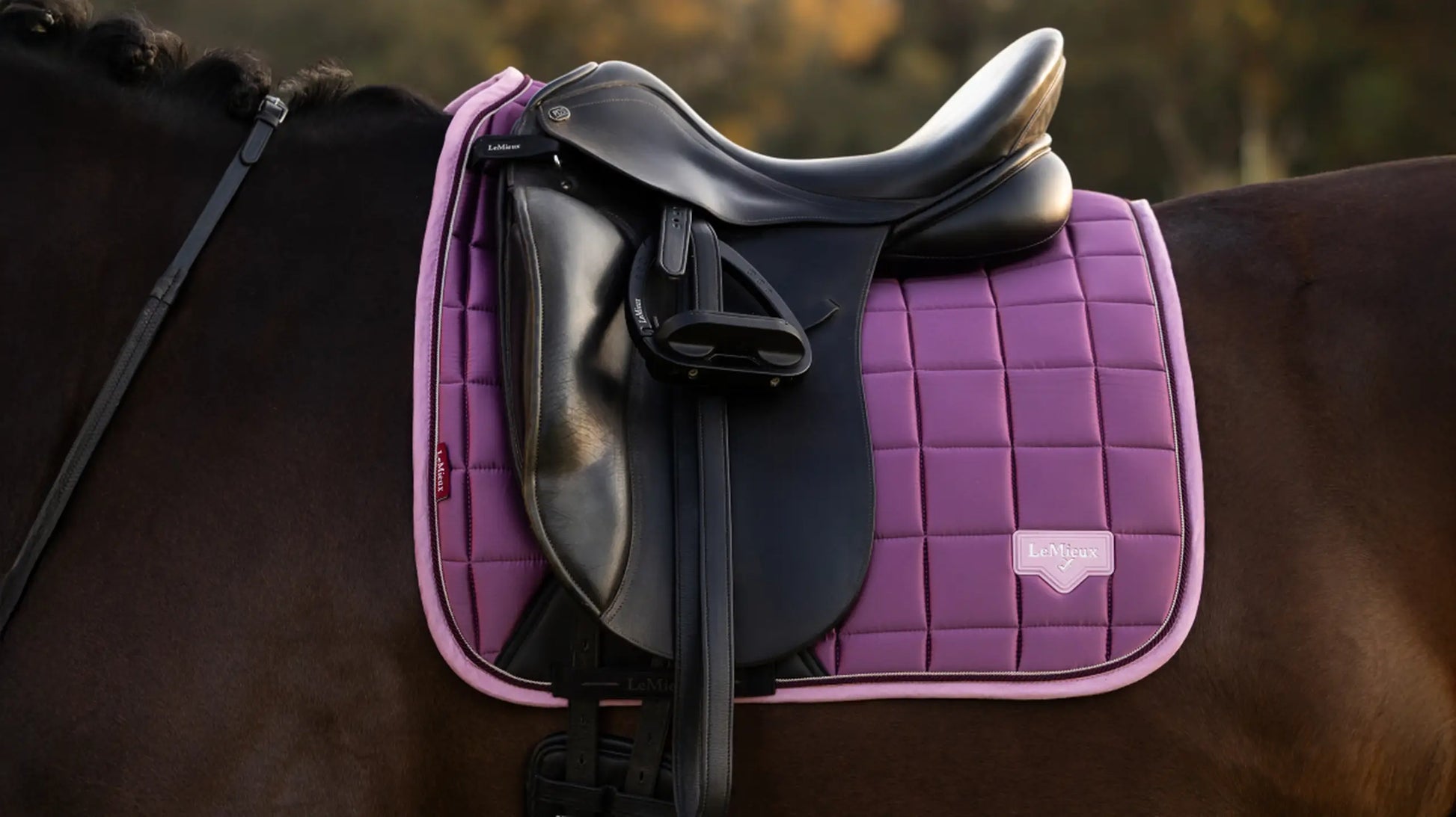 A close-up of the LeMieux Loire Dressage Saddle Pad in Mallow Purple, showing the luxurious satin finish, signature woven label, and quilted honeycomb pattern.