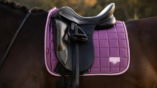 A close-up of the LeMieux Loire Dressage Saddle Pad in Mallow Purple, showing the luxurious satin finish, signature woven label, and quilted honeycomb pattern.