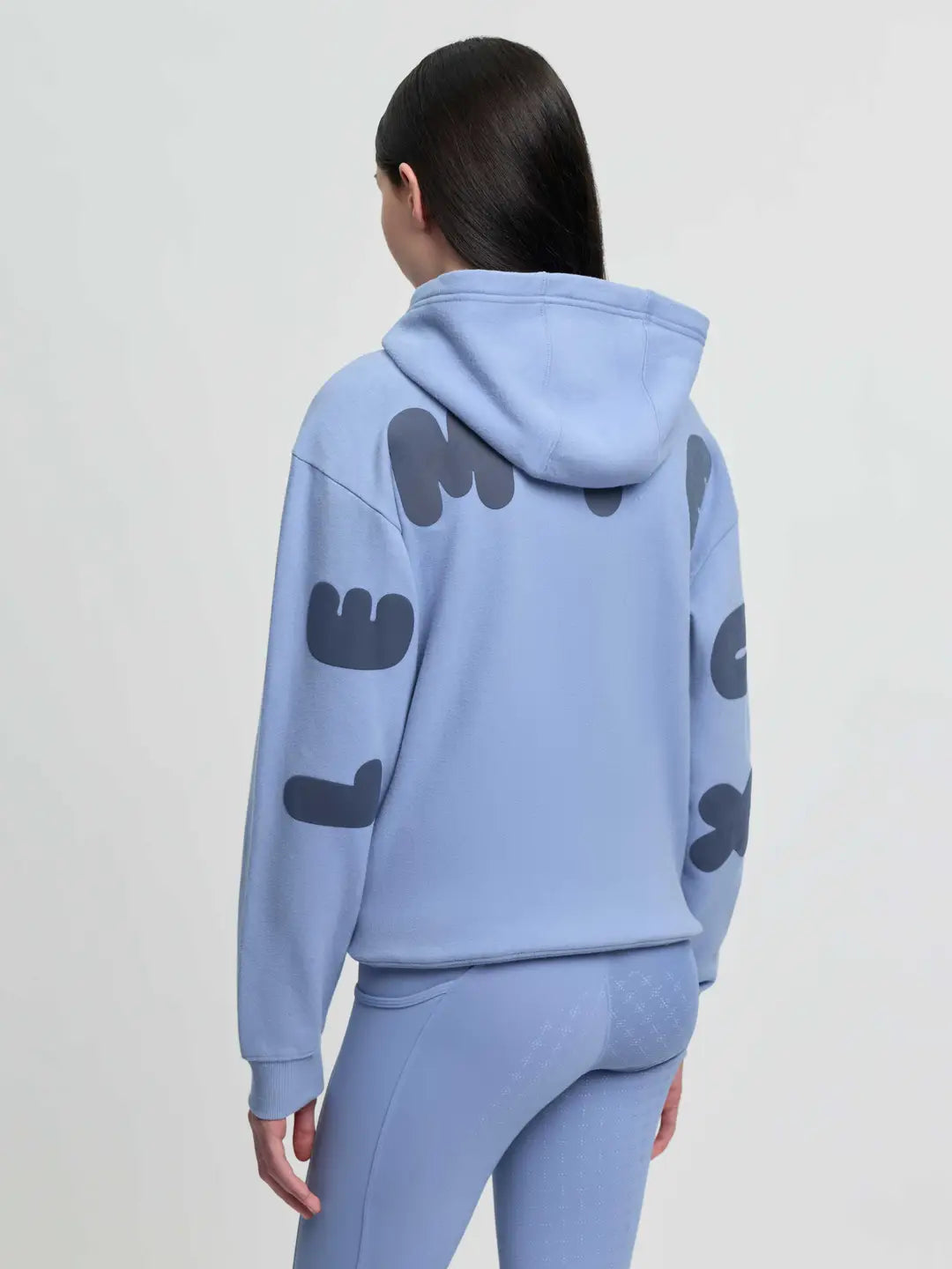 A junior rider wearing a soft Powder Blue LeMieux Sia hoody with front pockets and LeMieux logo on back